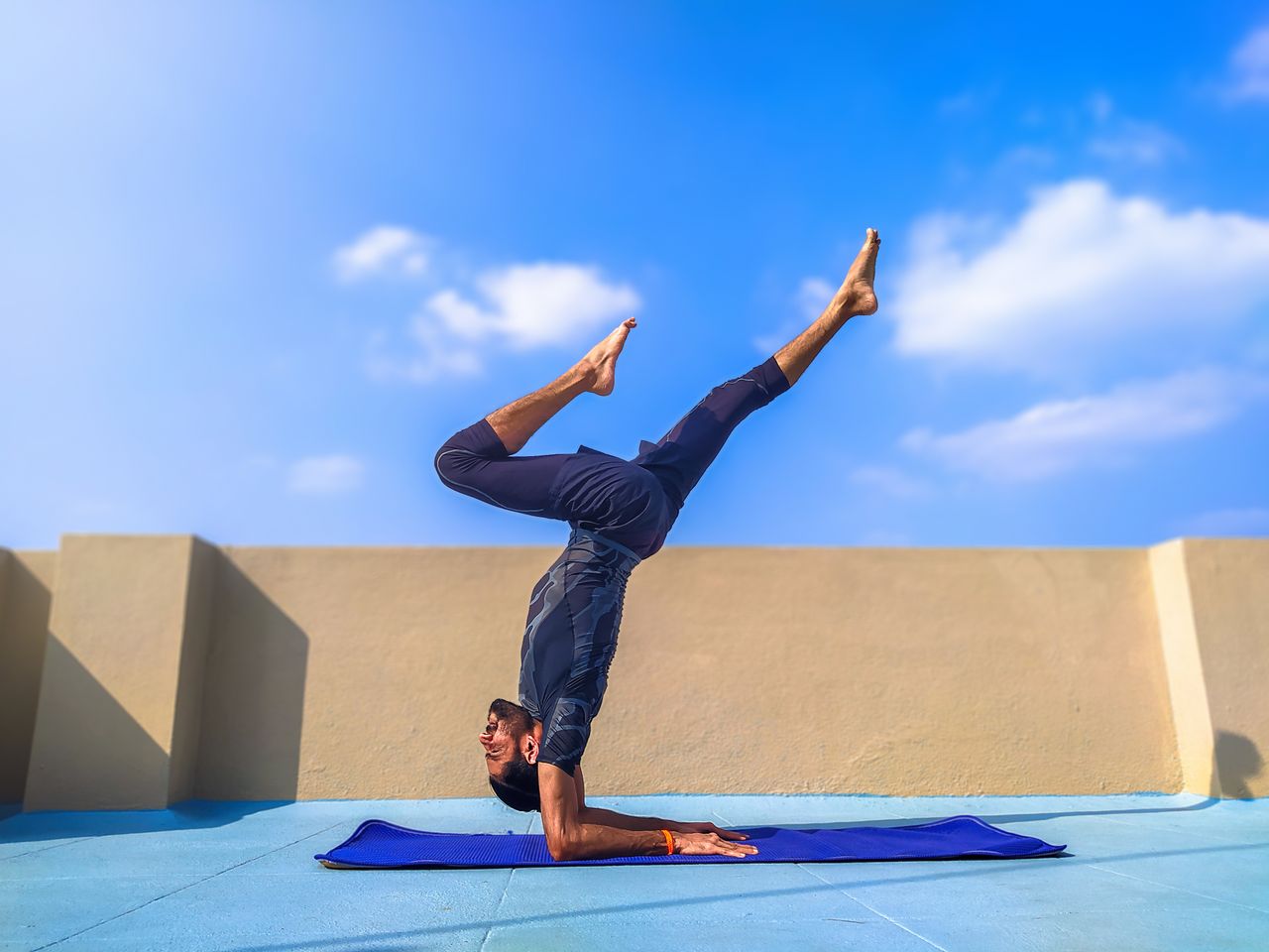 Adult man in yoga pose on rooftop with a bright blue sky background. Ideal for fitness content.