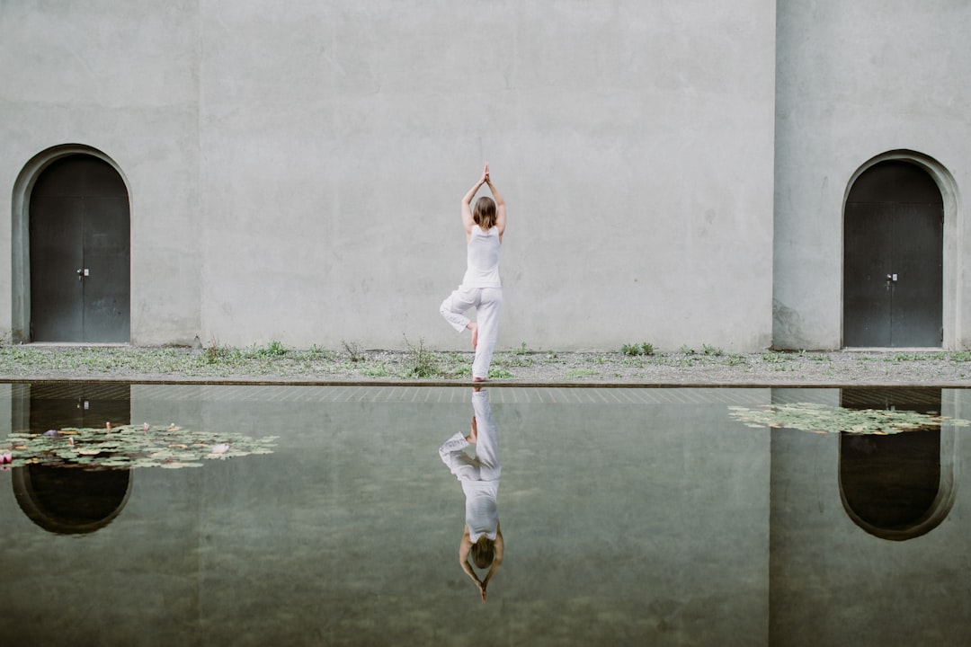 Woman in white clothing performing yoga pose in front of a pond with water lilies