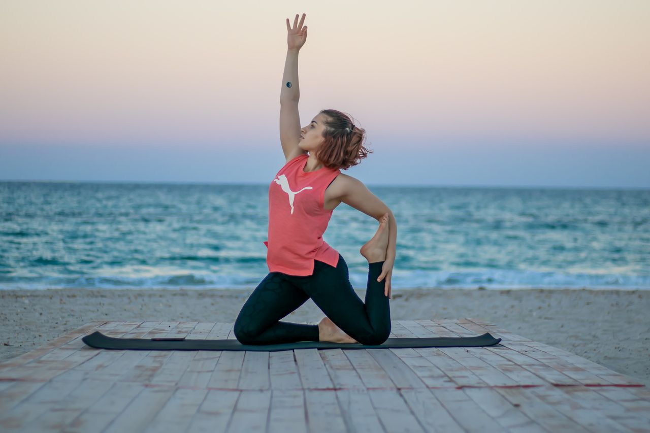 Woman practicing yoga by the sea at sunset in Mahdia, Tunisia, promoting relaxation and fitness.